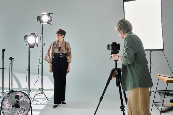 A middle-aged photographer captures her partner as she strikes a pose in a photo studio. - Photo, Image