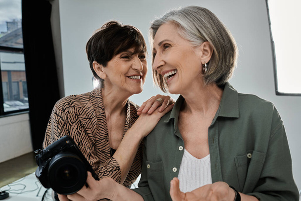 Twee vrouwen van middelbare leeftijd, een fotograaf en een model, glimlachend en met een camera in een fotostudio. - Foto, afbeelding