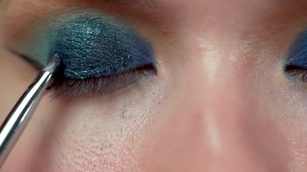 Detailní záběr modrého očního stínidla nanášeného na oční víčka pomocí štětce na líčení s třpytivou povrchovou úpravou. Detailní záběr - Záběry, video