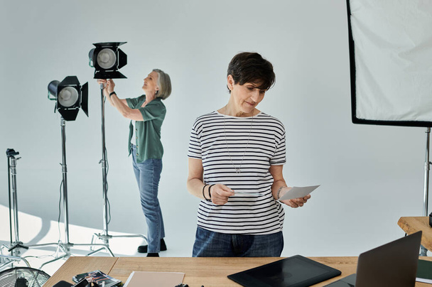 Kobieta w średnim wieku i jej kolega stoją ramię w ramię w nowoczesnym studiu fotograficznym, gotowi do wspólnej pracy nad projektem. - Zdjęcie, obraz