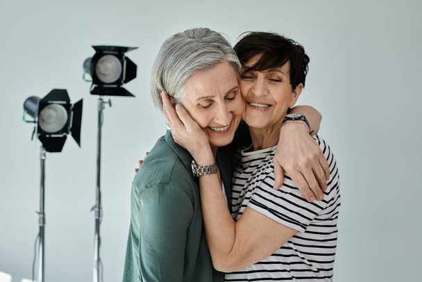 Zwei Frauen mittleren Alters umarmen sich vor einer Kamera in einem professionellen, modernen Fotostudio-Setting. - Foto, Bild