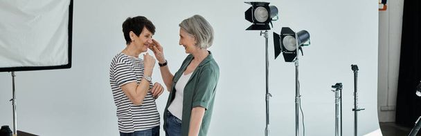 Una pareja de lesbianas de mediana edad posa con confianza para una cámara en un moderno estudio fotográfico. - Foto, Imagen