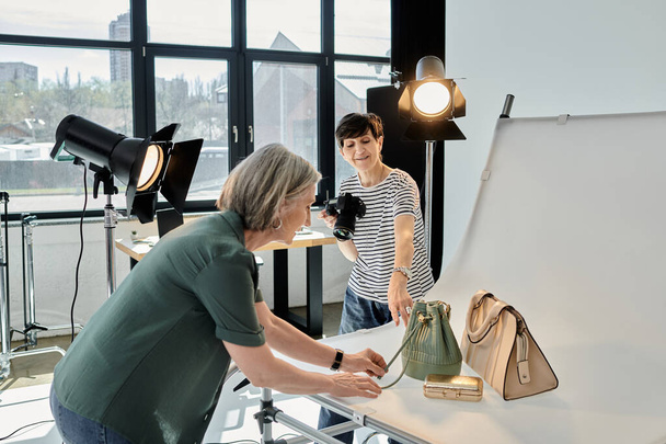 Пара средних лет, работающая в профессиональной фотостудии, пока одна женщина фотографирует сумки - Фото, изображение