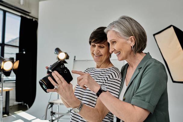 İki orta yaşlı kadın profesyonel bir fotoğraf stüdyosunda fotoğraf makinesiyle bir anı yakalıyor.. - Fotoğraf, Görsel