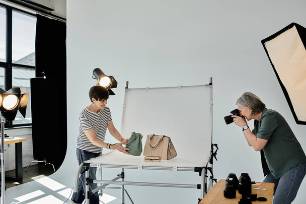 カメラマンは現代的なスタジオの設定でカメラのレンズを通してファッションバッグをキャプチャします. - 写真・画像