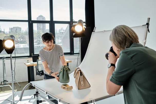Una mujer de mediana edad toma una foto de monederos en un entorno profesional de estudio fotográfico. - Foto, imagen