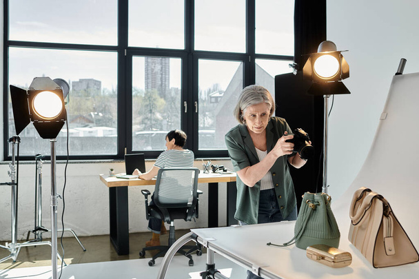 Een vrouw van middelbare leeftijd maakt een foto van handtassen in een moderne fotostudio opstelling. - Foto, afbeelding