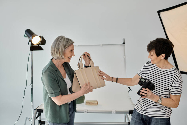 Una pareja de lesbianas de mediana edad en un estudio fotográfico profesional, una con una bolsa y la otra con una cámara. - Foto, imagen