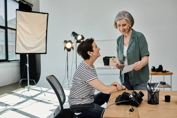 Una mujer de mediana edad se sienta en un escritorio en un estudio moderno profesional, trabajando juntos. - Foto, imagen