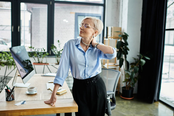 Een middelbare leeftijd zakenvrouw met kort haar werken ijverig aan een bureau, zich onwel voelen tijdens de menopauze. - Foto, afbeelding