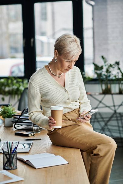 Empresaria de mediana edad con el pelo corto disfruta de un momento de relajación, tomando café en una oficina moderna. - Foto, Imagen