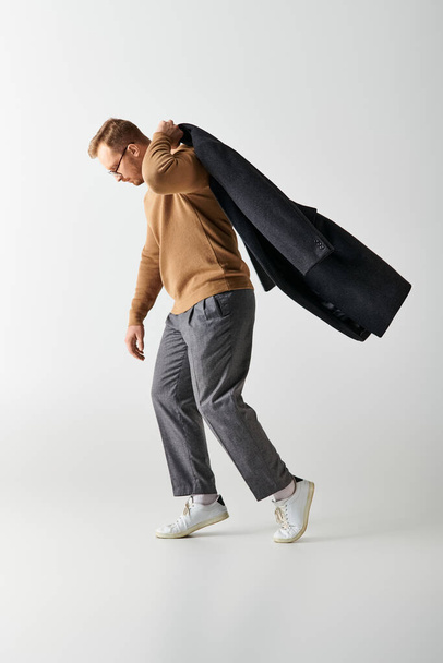A fashionable man in stylish clothing walking energetically while carrying coat. - Фото, изображение