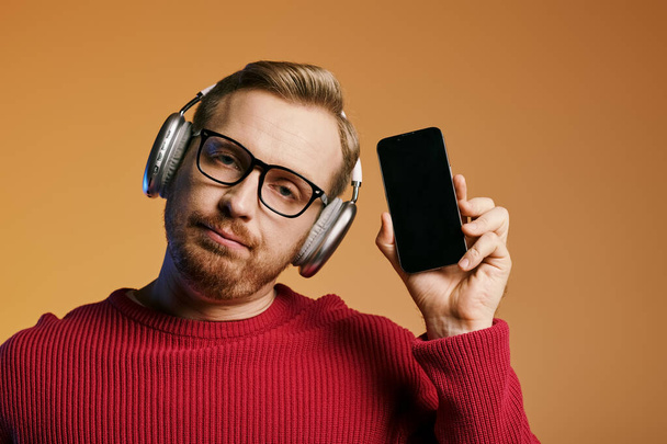 Ein stilvoller Mann hört Musik über Kopfhörer, während er ein Handy in der Hand hält. - Foto, Bild