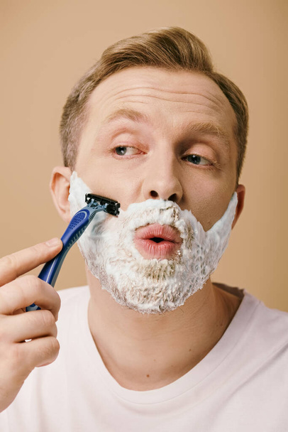 Ένας άντρας με περιστασιακή ενδυμασία ξυρίζει το πρόσωπό του με ξυράφι.. - Φωτογραφία, εικόνα