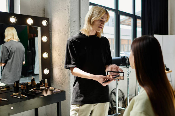 Une femme debout devant un miroir tandis qu'un maquilleur travaille sur son visage. - Photo, image