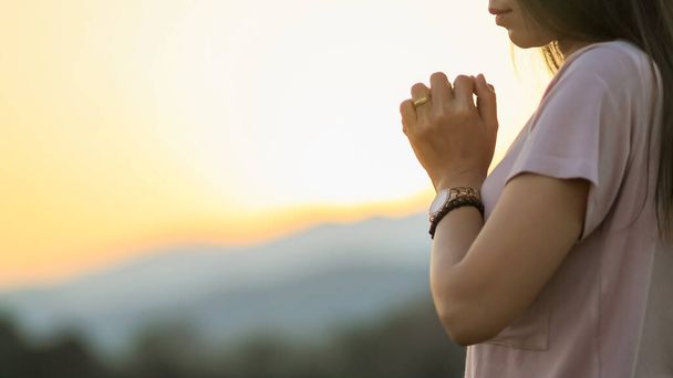 young woman clasped her hands together in prayer asking for forgiveness from God based on her Christian beliefs and faith in God teachings. concept prayer and intercession according beliefs about God - Photo, Image