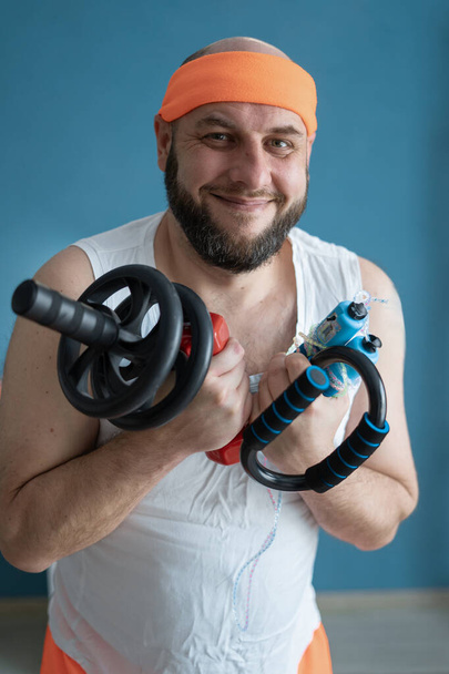 Ένας άντρας με στολή γυμναστικής χαμογελά και κρατάει τον εξοπλισμό γυμναστικής, προωθώντας την καλή φυσική κατάσταση και ευεξία με χαρούμενο τρόπο - Φωτογραφία, εικόνα