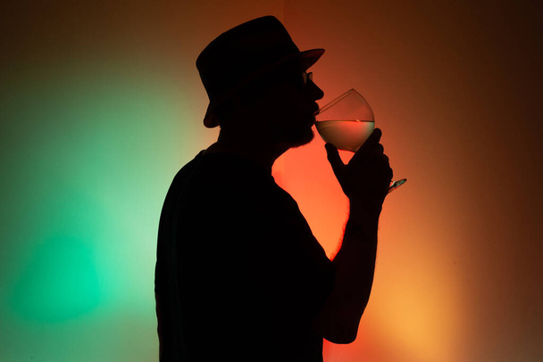 Ritratto di un uomo non identificato in silhouette che beve liquido da un vetro trasparente. Isolato su sfondo colorato. - Foto, immagini