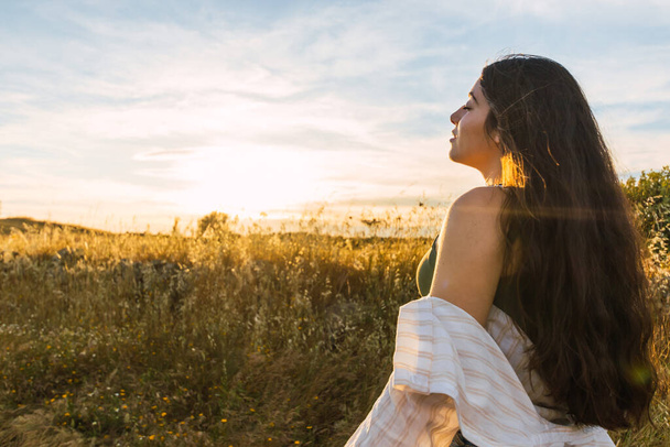 attractive brunette woman portrait on a field during sunset. side view - Photo, Image