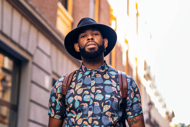 Stílusos fekete férfi alternatív hipszter megjelenés sétál az utcákon egy város egy napos nyári napon. boldogan mosolyog. - Fotó, kép