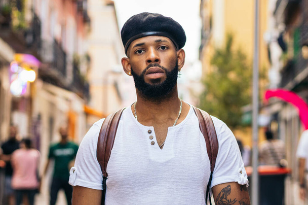 Portrét stylového černocha s baretem a tetováním stojícího na městské ulici a hledícího do kamery - Fotografie, Obrázek