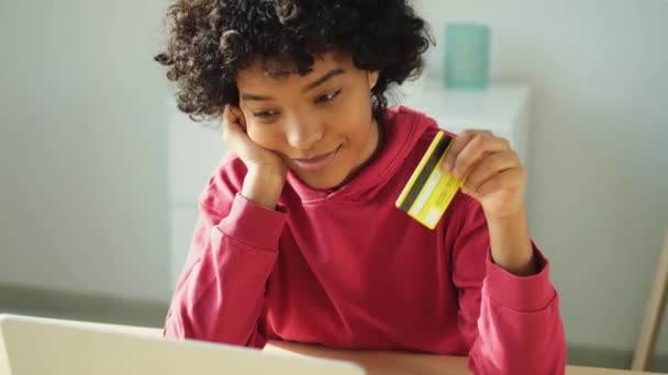 Egy afro-amerikai nő, aki laptopot vásárol online, aranykártyával fizet. Lány otthon ül vásárol az interneten adja meg a hitelkártya adatait. Online vásárlás e-kereskedelmi szállítási szolgáltatás - Felvétel, videó