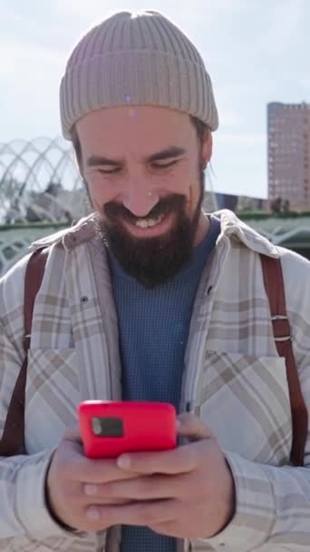 Vertical. Bonito homem caucasiano sorrindo usando móvel no parque de ciência cidade de Valência. Jovem turista alegre de pé feliz falando no telefone celular no dia ensolarado. Homem a atender uma chamada. Turismo cultural - Filmagem, Vídeo