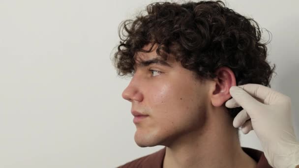 4k videó Sebész orvos megvizsgálja fül férfi beteg előtt otoplasztikai műtét. Kozmetikai fülműtét előtti elkészítése, a fül alakjának, helyzetének vagy méretének megváltoztatására irányuló eljárás. - Felvétel, videó