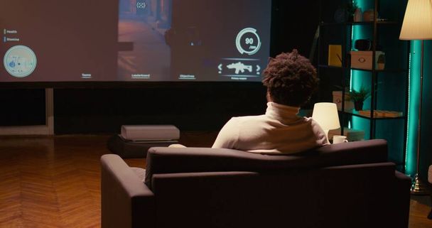 Mies pelaa ampuja videopeli televisiossa ase ammunta laser luoteja lentävät robotit pimeässä ilmakehän teollisuusympäristössä. Gamer nauttia kilpailukykyinen PvP fps internet moninpeliturnaus peli - Valokuva, kuva