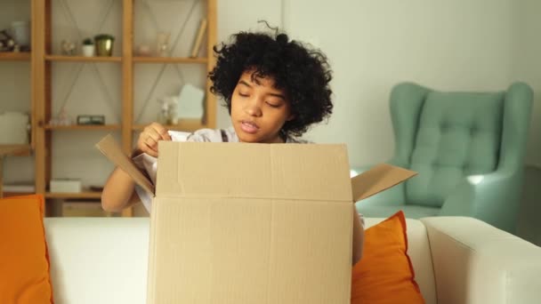 Paketleri açan Afrikalı kız kutuya bakıyor. Kutuyu açan mutlu kadın. Paket teslim edilen eşyalara bakan bir kadın. Tatmin olmuş istemci olumlu geri bildirim hızlı teslimatı - Video, Çekim