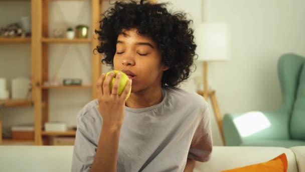 Evde yeşil elma yiyen mutlu güzel kız. Güzel Afro-Amerikan genç bayan taze meyve yiyor ve gülümsüyor. Sağlıklı gıda vejetaryen diyet konsepti. Sağlıklı atıştırmalıklar. - Video, Çekim