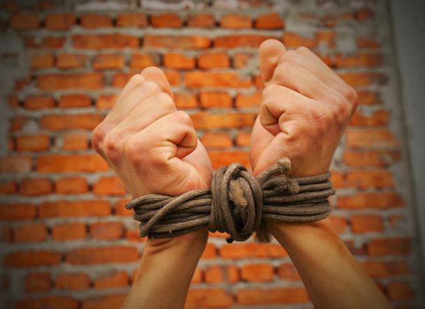 Mains liées par une corde contre un mur de briques
 - Photo, image