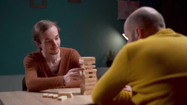 Two men are deeply engrossed in a game of Jenga, savoring their leisure time in a cozy indoor setting. Copy space - Séquence, vidéo