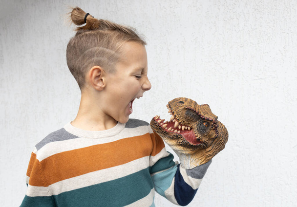 child plays with scary toy head of dinosaur, putting it on hand, scaring it with terrible grimace. Develop imagination and courage in children. boy studies ancient reptiles. Don't be afraid, be brave - Photo, Image