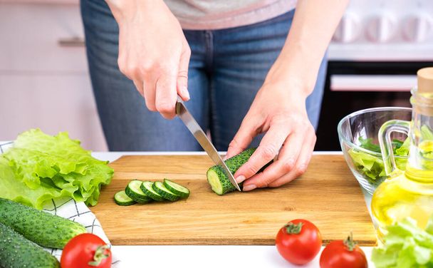 Mujer joven corta pepinos y cocinar ensalada de verduras. Concepto de dieta y alimentación saludable. - Foto, imagen