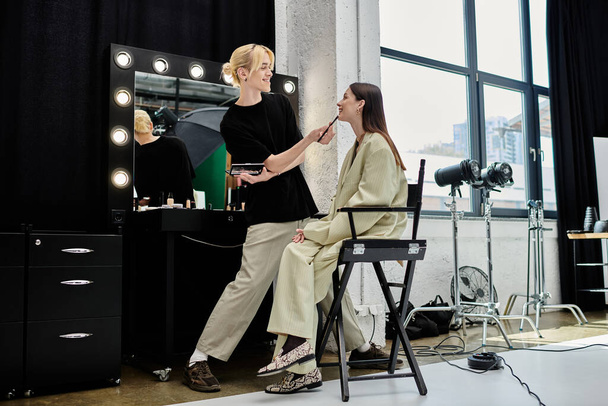 Γυναίκα κάθεται μπροστά καθρέφτη ως καλλιτέχνης μακιγιάζ εφαρμόζει. - Φωτογραφία, εικόνα