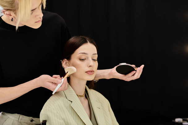 Een make-up artiest brengt sierlijk make-up aan op een vrouwengezicht met een kwast. - Foto, afbeelding