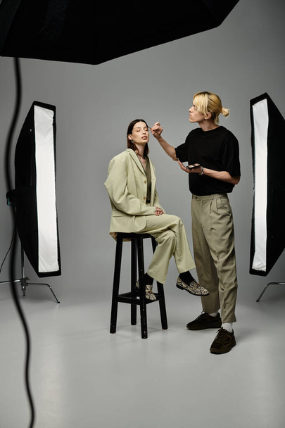 A woman sits on a stool, receiving makeup from a talented man. - Photo, Image
