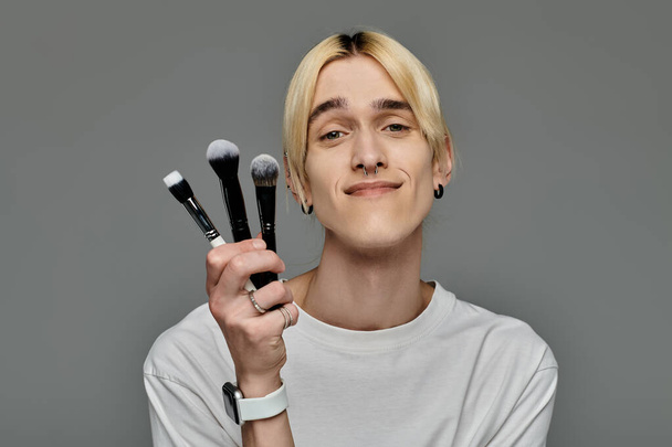 Un homme gay présentant une variété de pinceaux de maquillage. - Photo, image