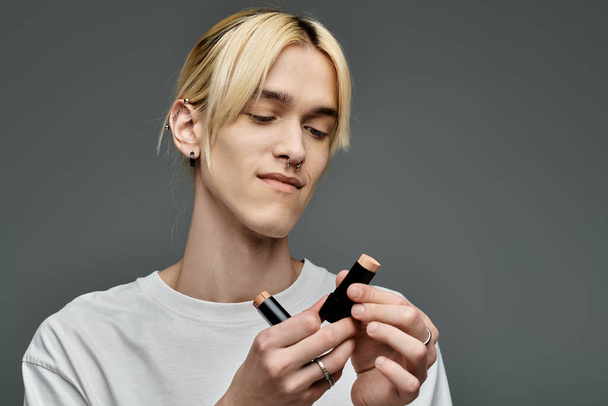Een man met blond haar kijkt naar make-up product. - Foto, afbeelding
