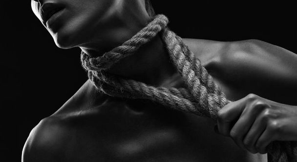 Молодая женщина вырывает веревки из своего тела и шеи. Фотография в черно-белом цвете - Фото, изображение