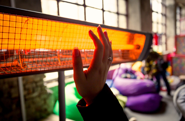 Gros plan de femme se réchauffant les mains à chauffage infrarouge
 - Photo, image