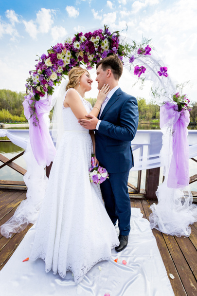 bride and groom hugging under decorated flower arch - Photo, Image