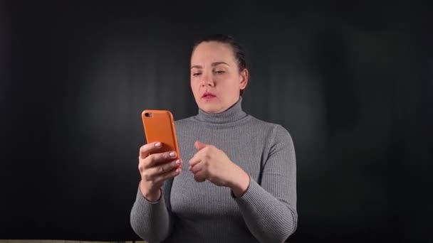 Портрет молодої жінки, що використовує мобільний телефон, взаємодіє з портативним інформаційним пристроєм на чорному тлі. Фокус та взаємодія, сучасне спілкування та технології в мінімалістичній обстановці - Кадри, відео
