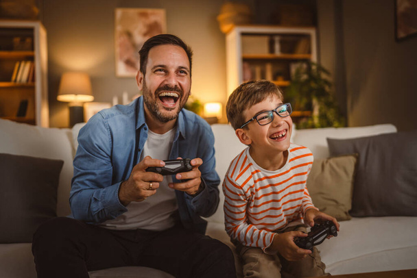 大人の慎重な父親と息子は自宅でジョイスティックでビデオゲームをプレイします - 写真・画像