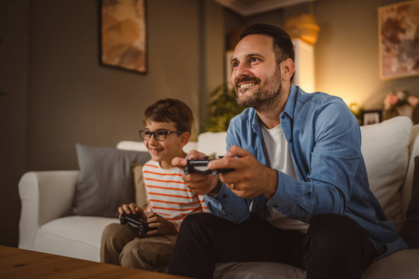 Erwachsene kaukasische Vater und Sohn spielen Videospiele mit Joystick zu Hause - Foto, Bild