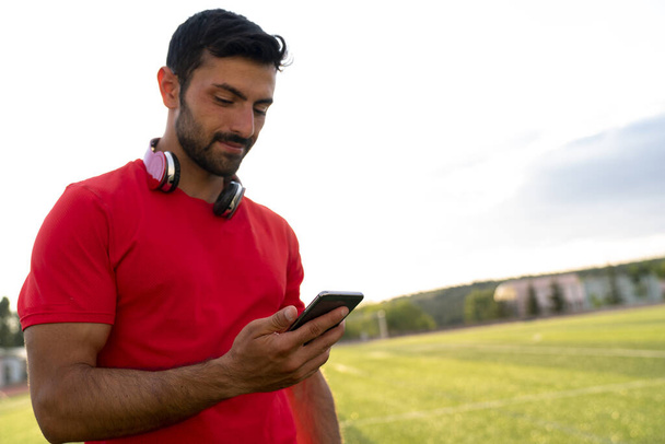 Egy férfi okostelefont használ a Városligetben, miután szabadtéri gyakorlatot végzett. Fitness sportoló férfi SMS nézi telefon képernyőn edzés után. - Fotó, kép