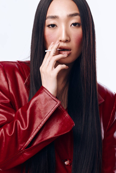 Rebellious woman with long black hair and red leather jacket smoking cigarette, isolated on white background - Photo, Image