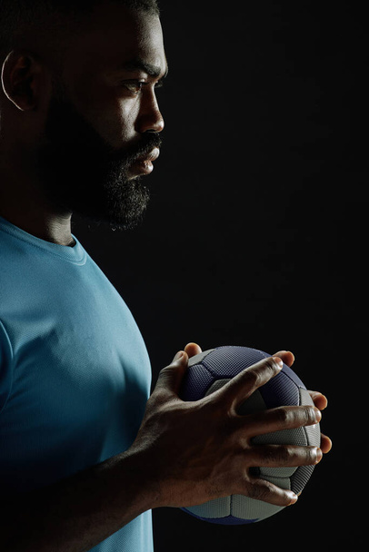 Podsvícený boční pohled detailní t na africký americký fotbalista drží míč proti černé pozadí kopírovat prostor - Fotografie, Obrázek