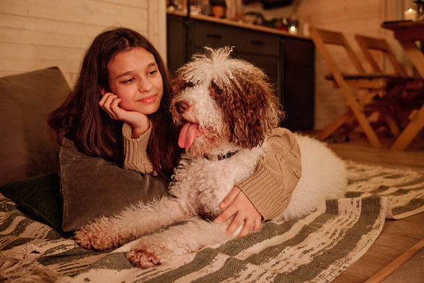 Menina adolescente feliz relaxando no chão na sala de estar, abraçando seu cão, desfrutando de noite de inverno em cabana de madeira, espaço de cópia - Foto, Imagem